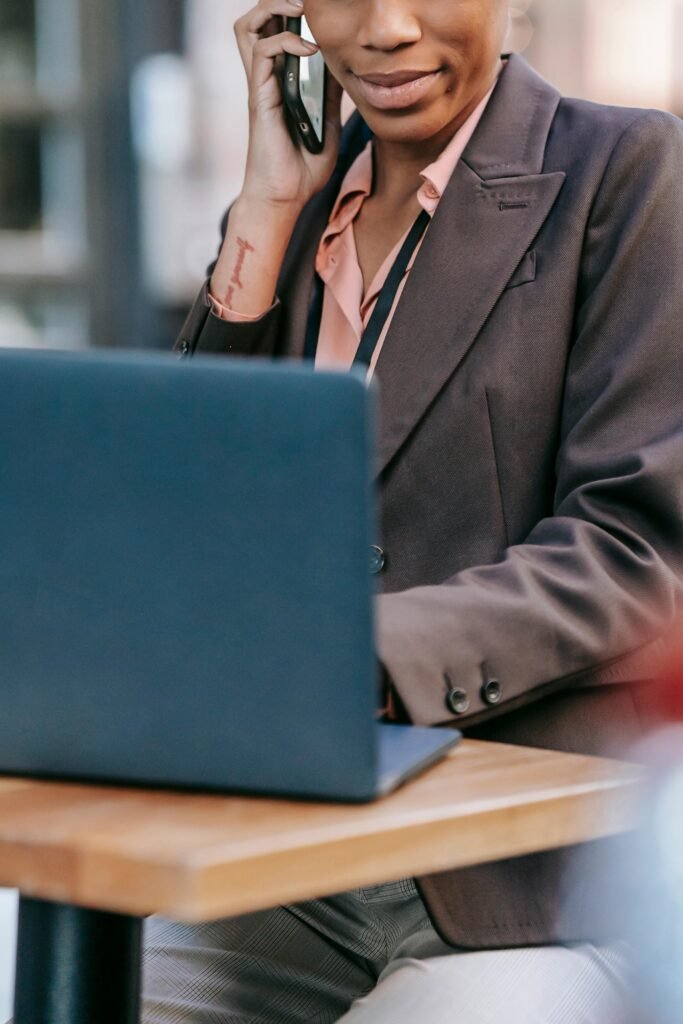 Young businesswoman multitasking at an outdoor café, speaking on phone and working on laptop.